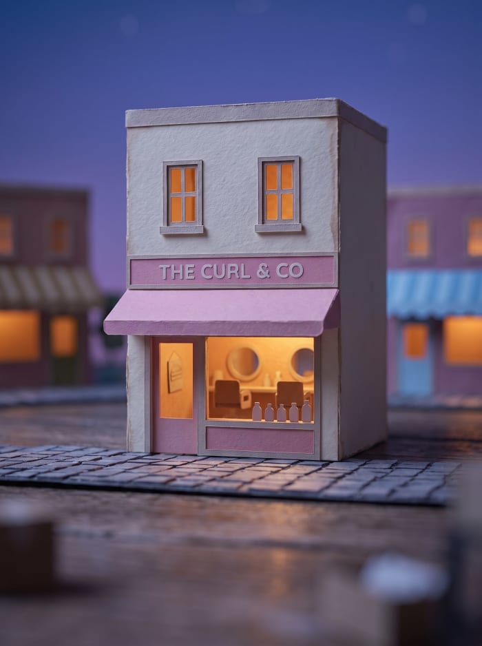 A model hair salon shopfront with a pink awning, lit at dusk.