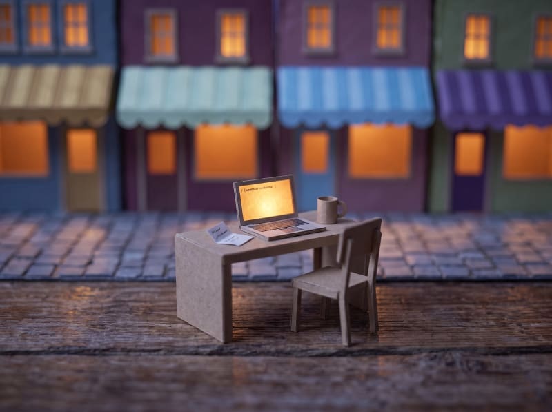 A tiny card laptop on a model desk, one line of code glowing on its screen.