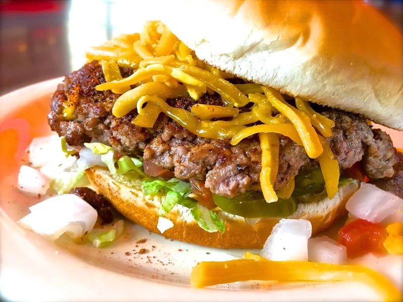 A Hut's burger with shredded cheddar, shredded lettuce, pickles, and diced onion on a plain bun