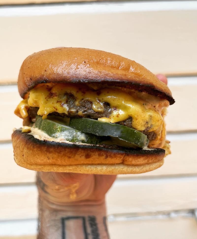 The Le Beef Burger held up in one hand: a butter-toasted potato roll, melted American cheese, pickles, and pink special sauce