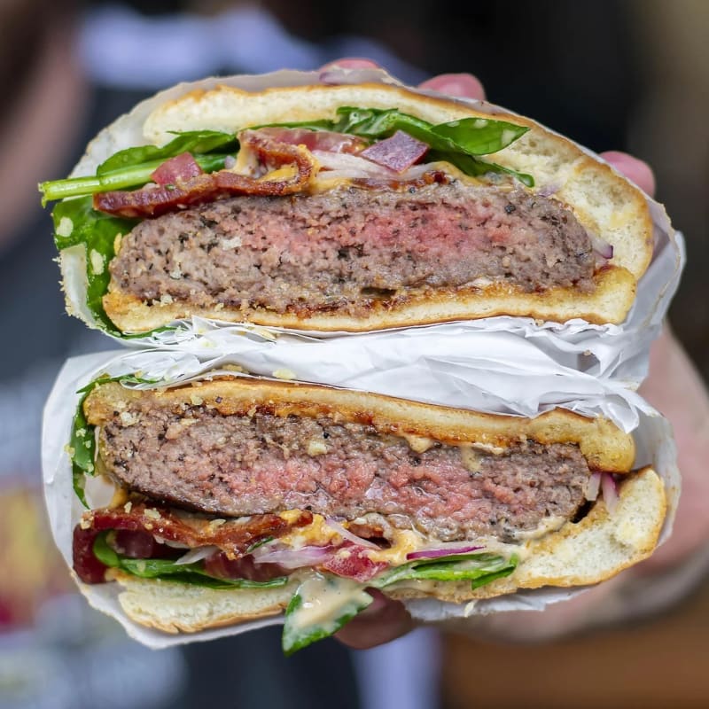 The Luke's Inside Out burger cut in half, showing a thick rare patty, bacon, spinach, red onion, and sauce on a toasted bun