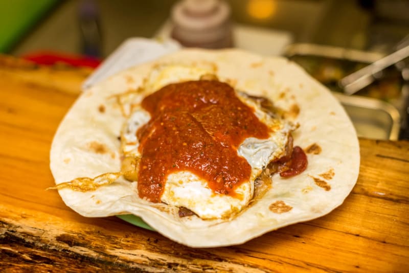 A Paco's Tacos breakfast taco on the wood counter: a fried egg and bacon on a flour tortilla, covered in red salsa