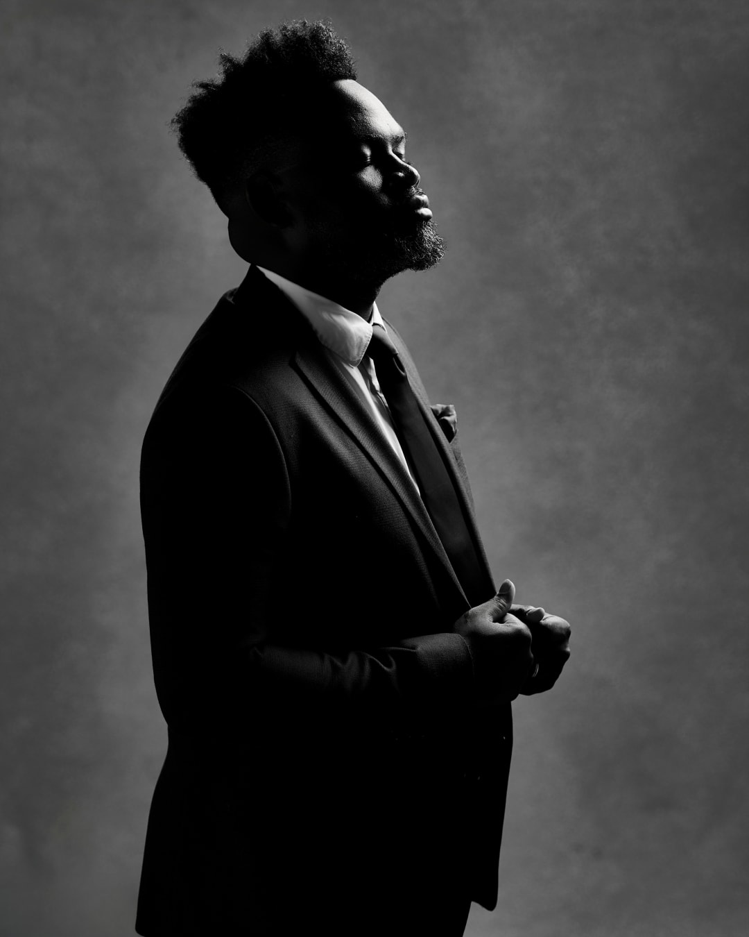 Chin lifted in black and white, a rim of light along the beard and collar