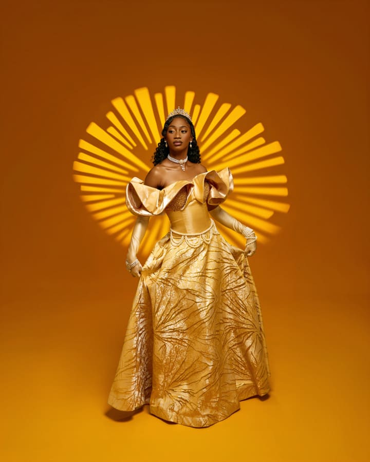 Divine in a gold gown and tiara against a gold backdrop, a sunburst of light behind her