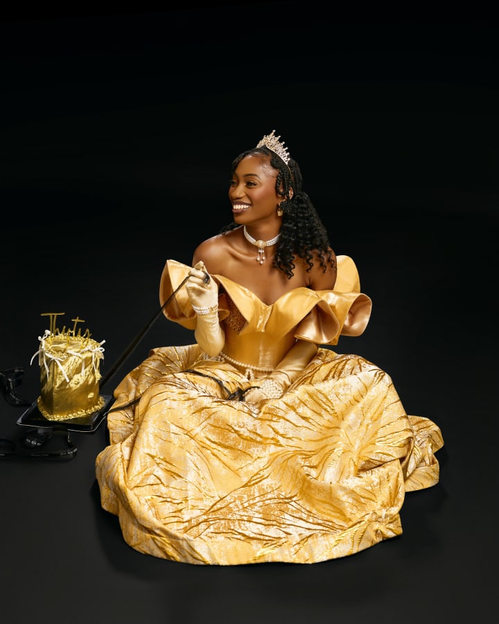 Seated on the floor in the gold gown, laughing, her birthday cake beside her