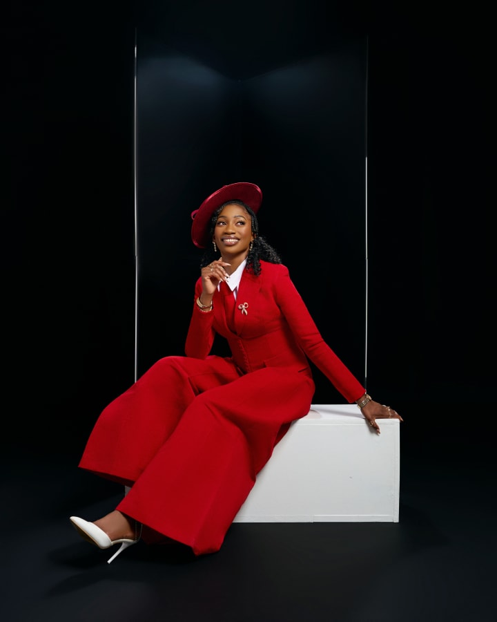 In a red suit and red hat, seated on a white plinth, smiling