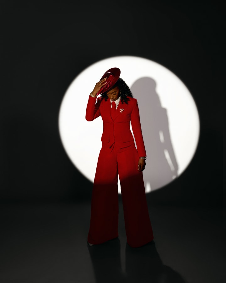 The red suit in a round spotlight, a hand shading her eyes