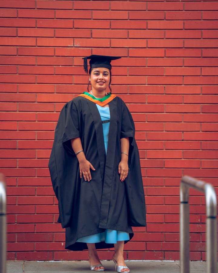 A graduate against a red brick wall, hands clasped