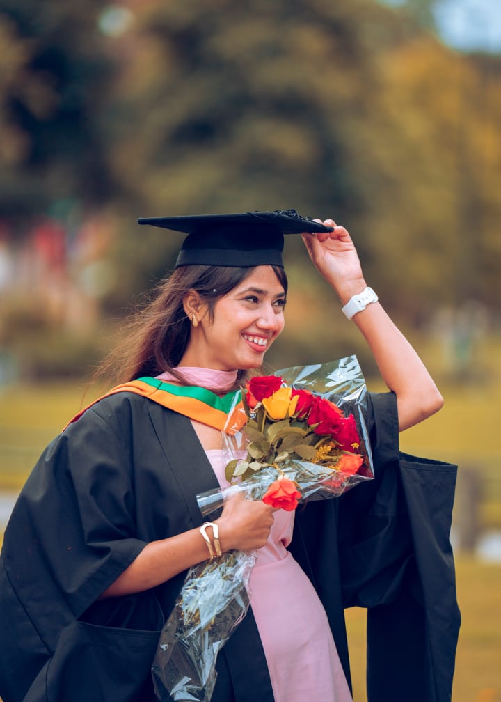 A graduate holding her cap on, a bouquet in the other hand