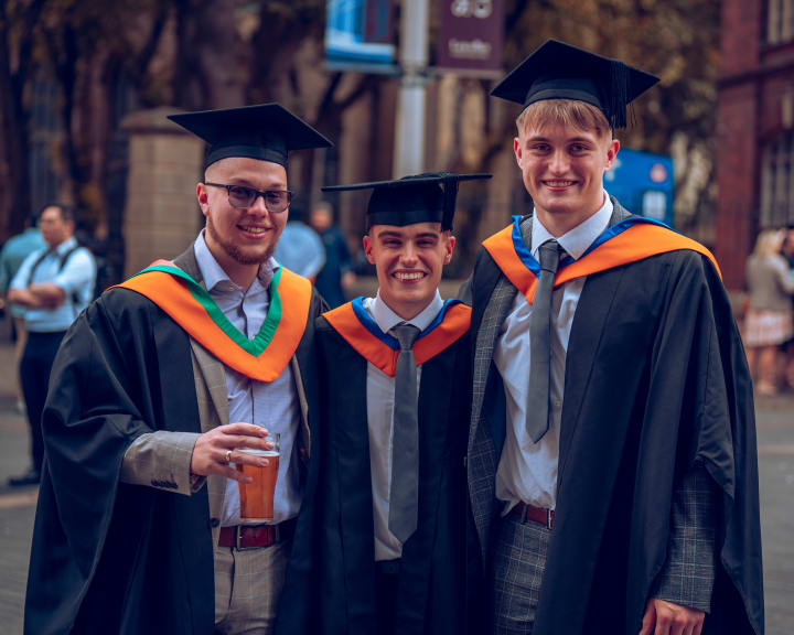 Three graduates laughing, orange hoods