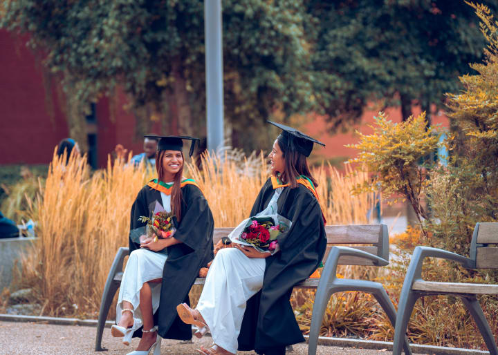 Two graduates on a bench among the grasses, bouquets on their laps