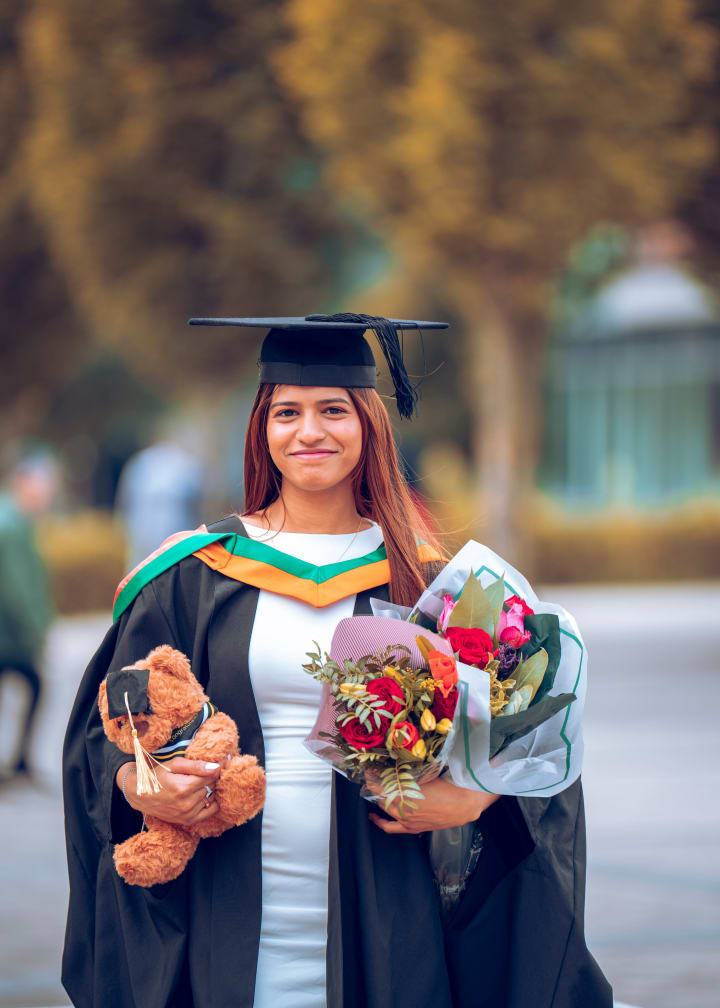 A graduate with a teddy and a bouquet, smiling