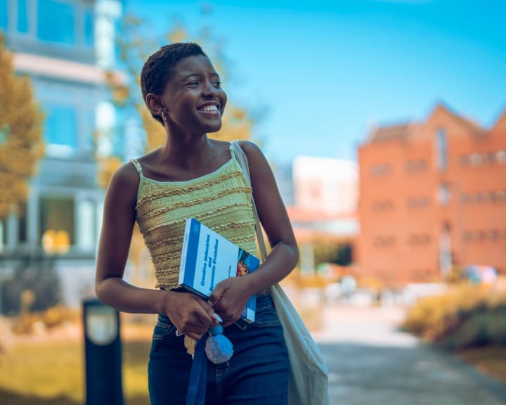Walking through campus, laughing, notebook in hand