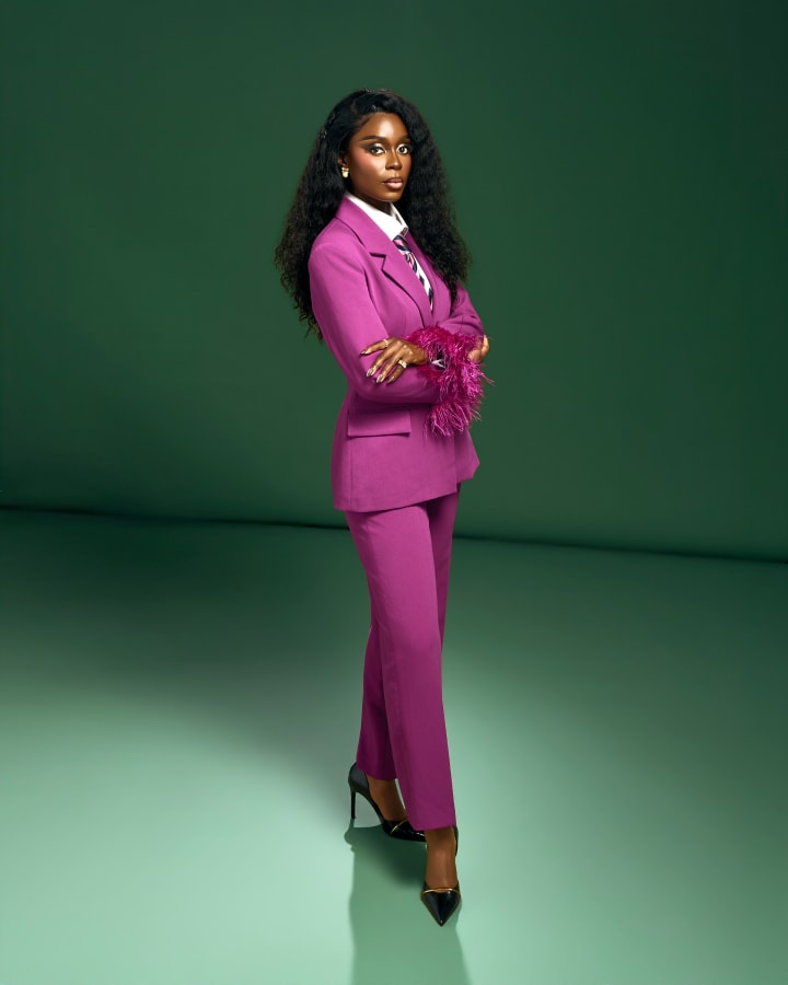 Standing against the green backdrop, arms folded, ankles crossed