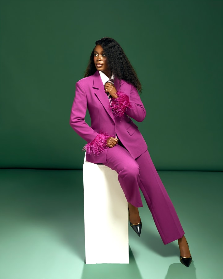 Perched on a white plinth, a hand at her tie, looking over her shoulder