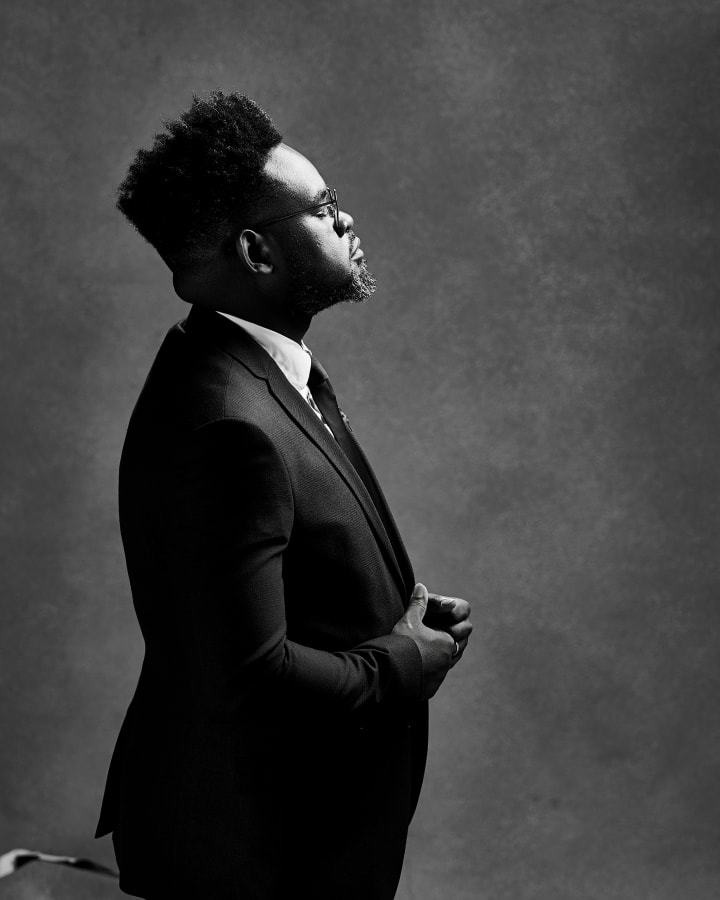 In profile in black and white, glasses on, the light on his face and hands