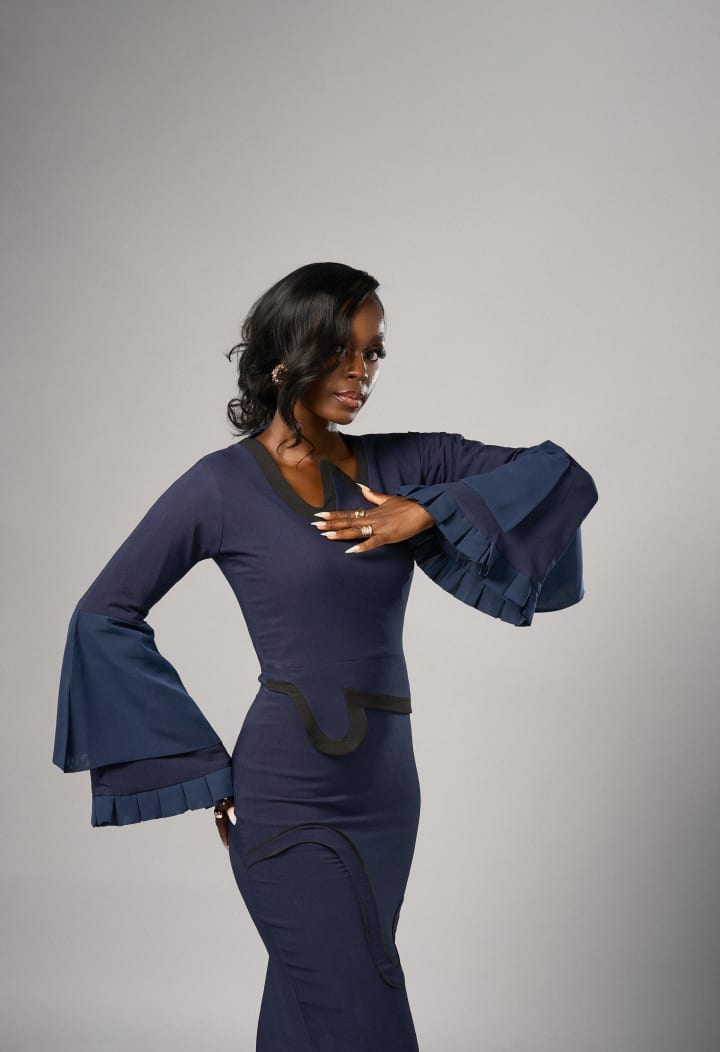 The navy dress with bell sleeves, one hand to the chest