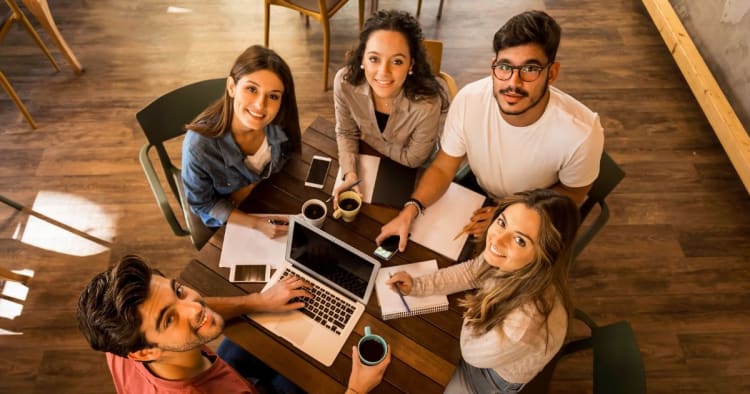 Five people learning at a table looking at the camera above.