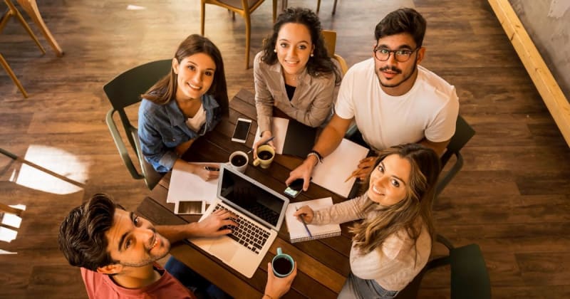 Five people learning at a table looking at the camera above.