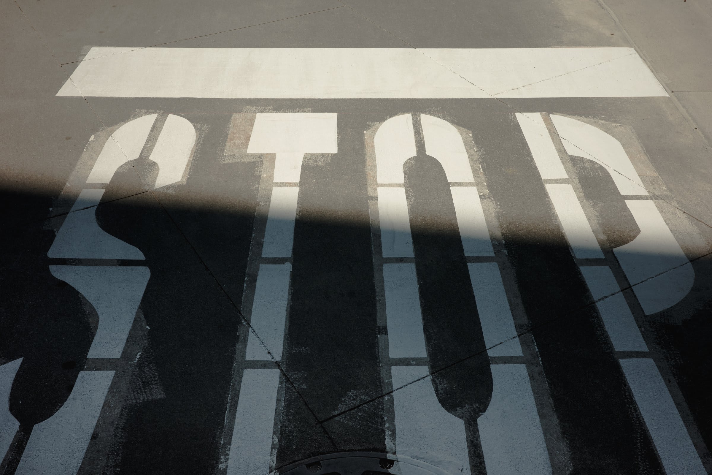 An overhead view of a metal grate with the word STOP painted in white, sun-bars cutting through the bars and casting striped shadows.