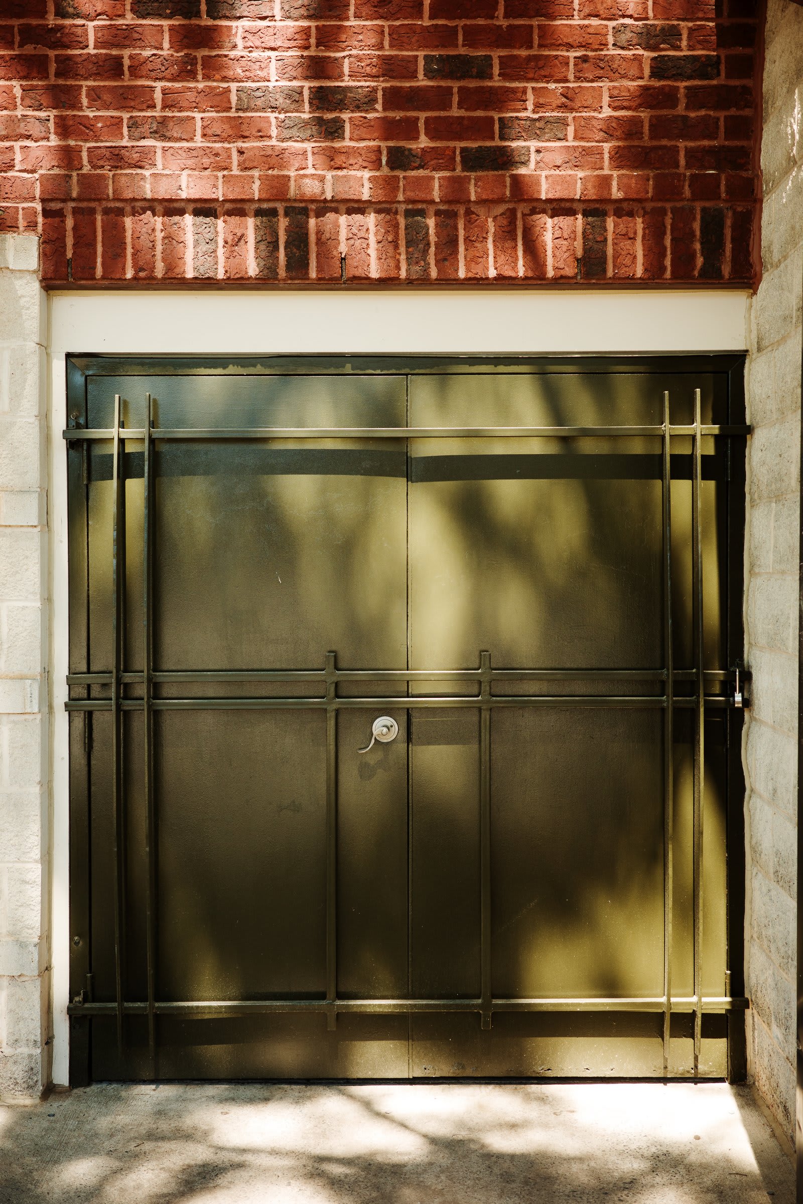 A recessed iron security gate set in a brick alcove, dappled tree shadows playing across the metal bars.