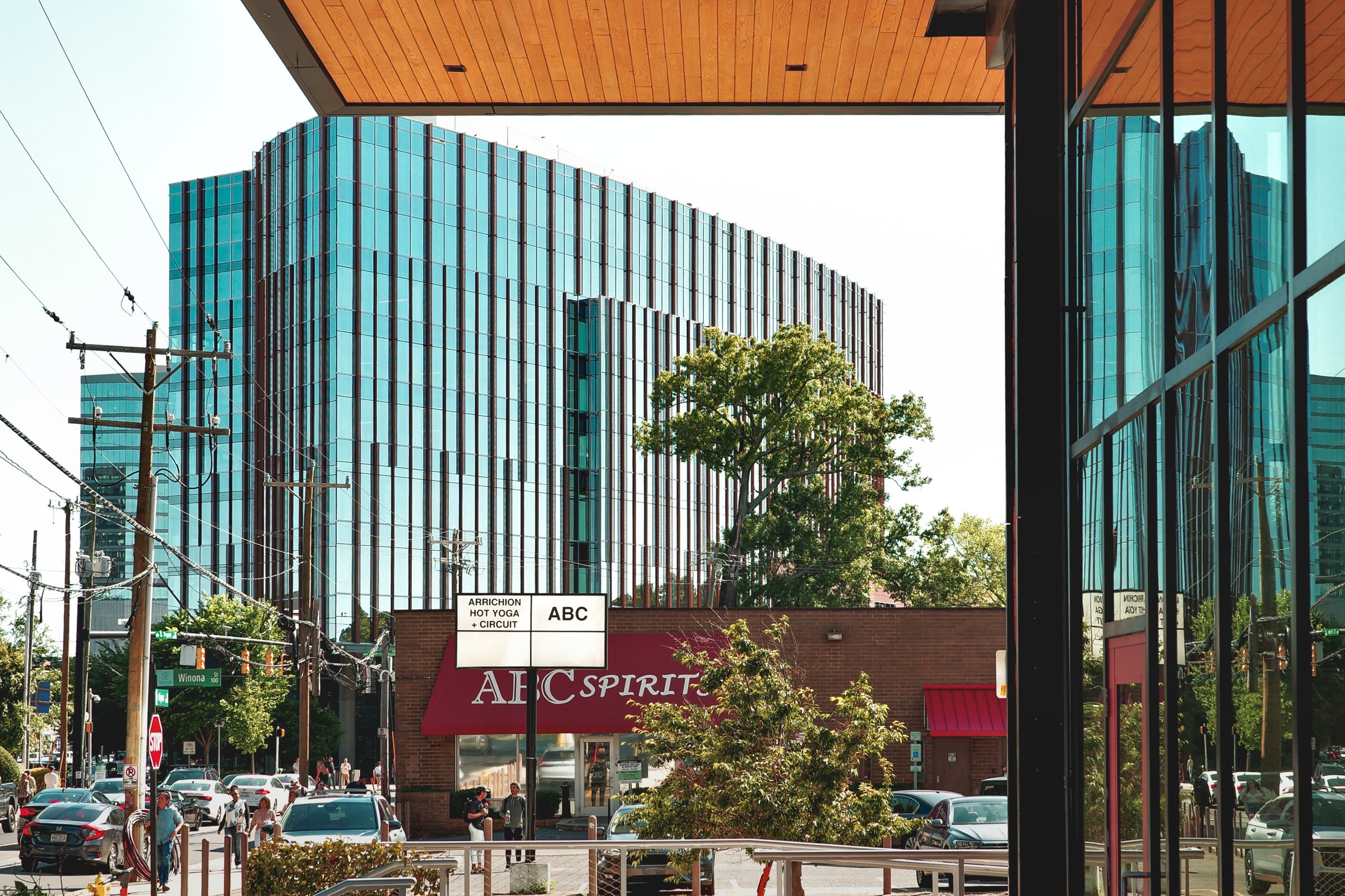 A street-corner view: an ABC Spirit liquor store with a red awning beneath a tall mirrored office tower that catches the afternoon sky in patches.