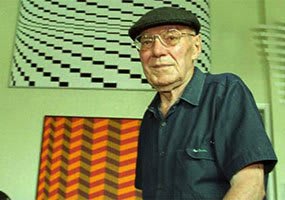Pintura a óleo retratando o artista Luiz Sacilotto em estúdio, com obras em andamento e materiais artísticos ao redor.