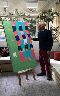 Retrato de Zi Facella, artista, com expressão serena e olhar direto, vestido com roupa clássica, em tons de cinza e azul.