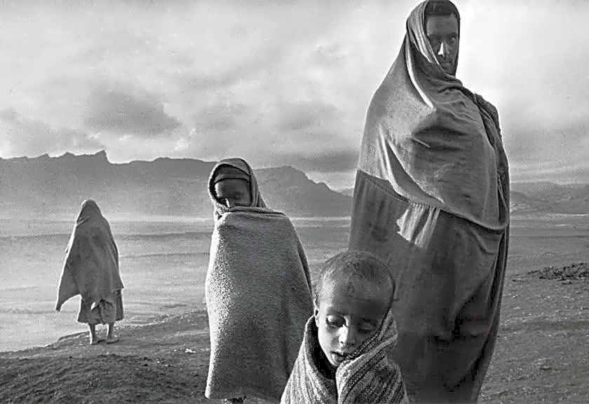 Fotografia em preto e branco de Sebastião Salgado em meio a uma paisagem de salinas, com tons de cinza e branco, retratando o trabalho de mineração de sal.