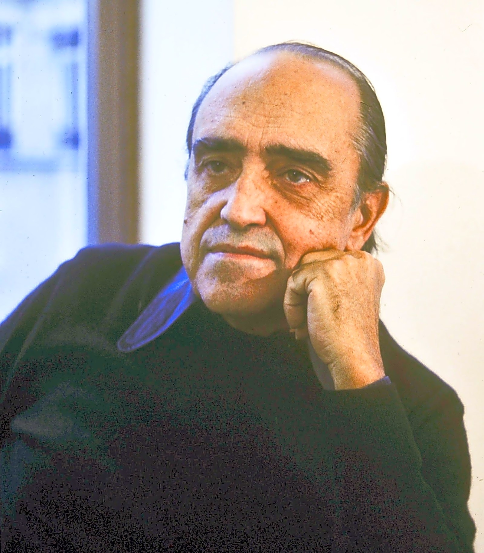 L'architecte brésilien Oscar Niemeyer, assis sur une chaise au design moderne, contemple une ville futuriste aux teintes bleues et argentées.