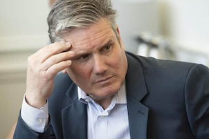 A photo of Keir Starmer in a suit, no tie, looking pensive with his hand on his forehead