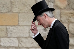 Jacob Rees-Mogg in a black suit and top hat, looking down, holding the tip of his hat