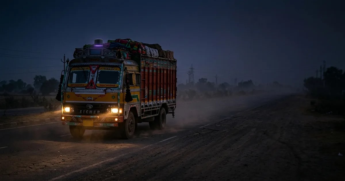A certified AIS-140 GPS tracker device being held in front of a commercial truck on an Indian highway, illustrating the new RTO rules for 2026