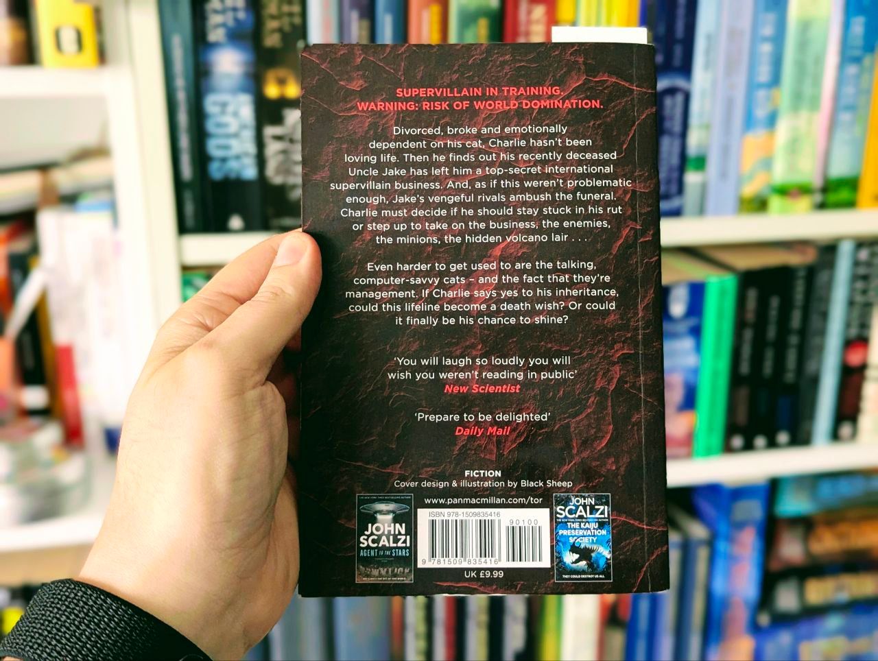 Eine Hand hält das Buch Starter Villain vor einem Bücherregal. Die Rückseite ist sichtbar.