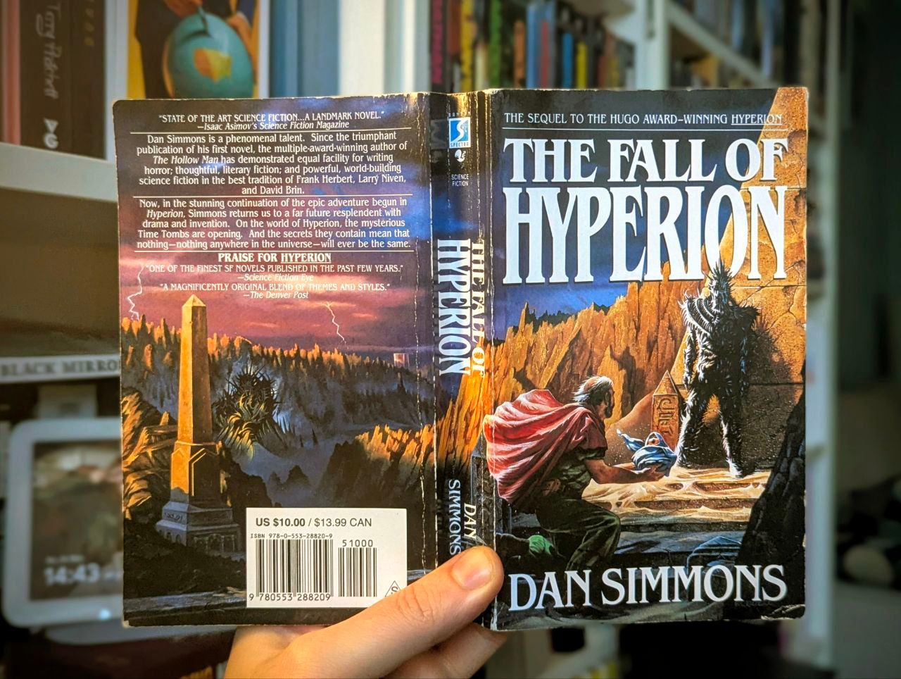 Schaut man sich das Cover an, würde man kaum erwarten, dass es sich hier um eine Mischung aus Space Opera, Science Fiction, Fantasy, Thriller und Cyberpunk handelt. Eine Hand hält das Buch The Fall of Hyperion hoch. Im Hintergrund ist ein Regal zu sehen.