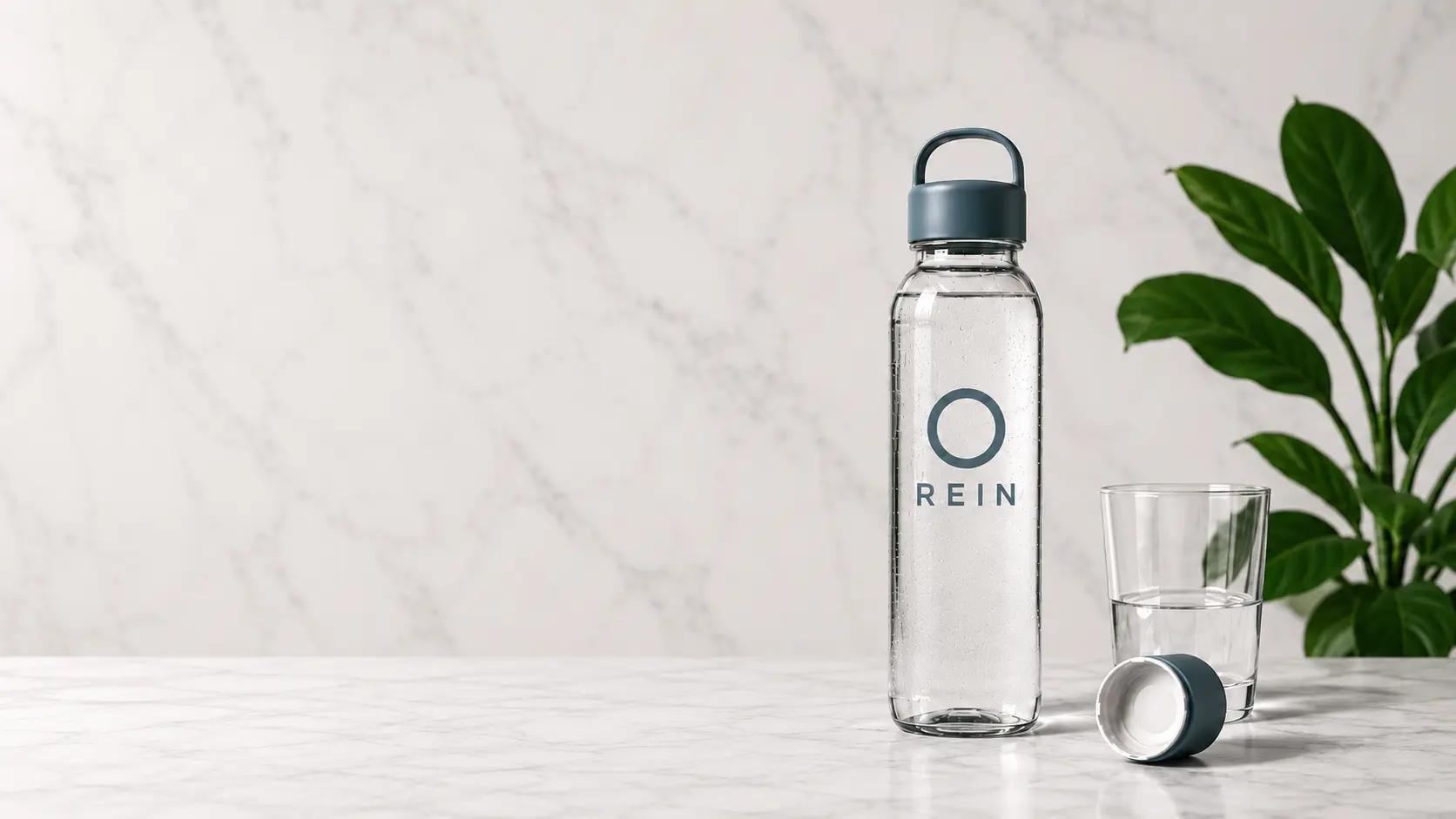 A REIN water bottle and glass of water on a marble surface beside a green plant