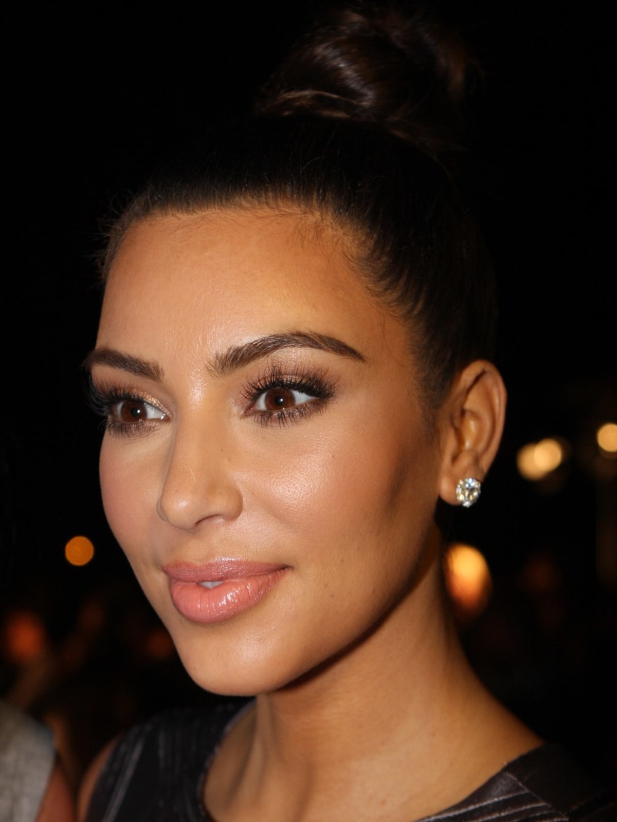 Kim Kardashian with a high bun, nude-pink lips and diamond stud earring in a close-up portrait from 2012