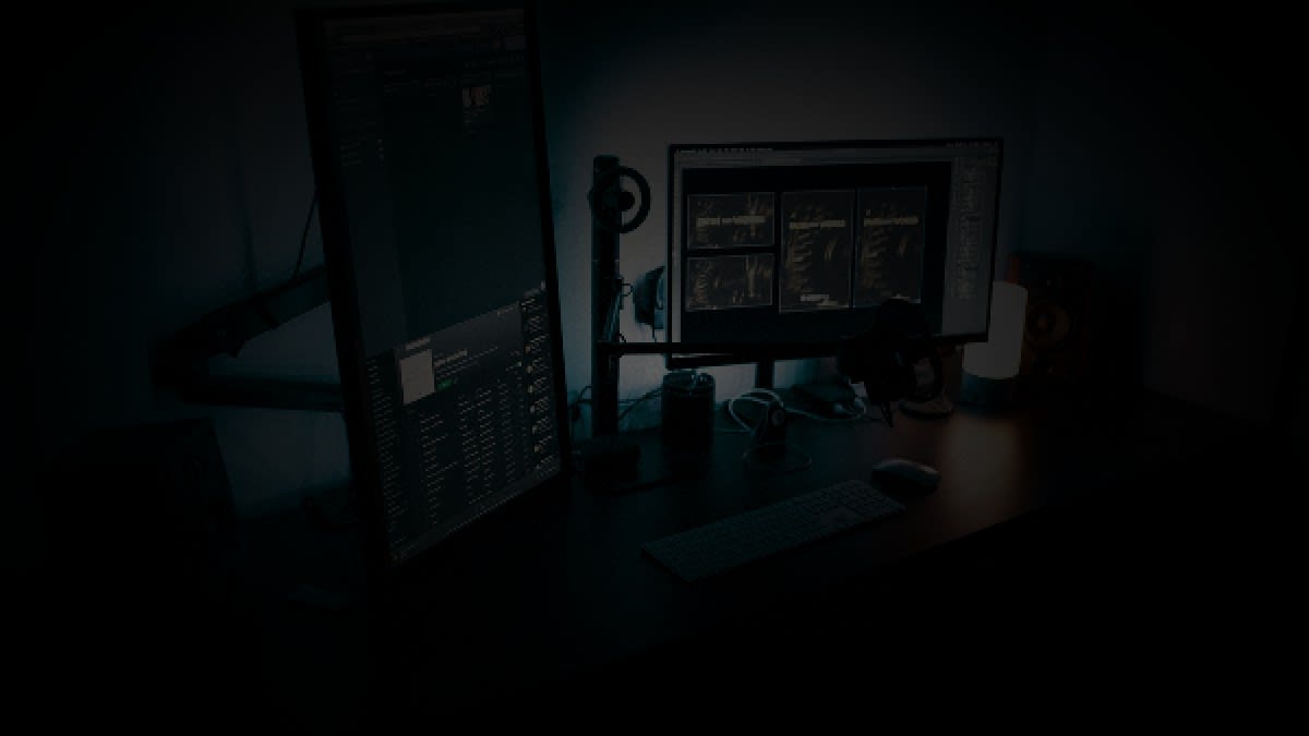 Photorealistic editorial photo of an empty high-tech dual-monitor desk at night with cool cyan backlight and warm desk lamp, no people.
