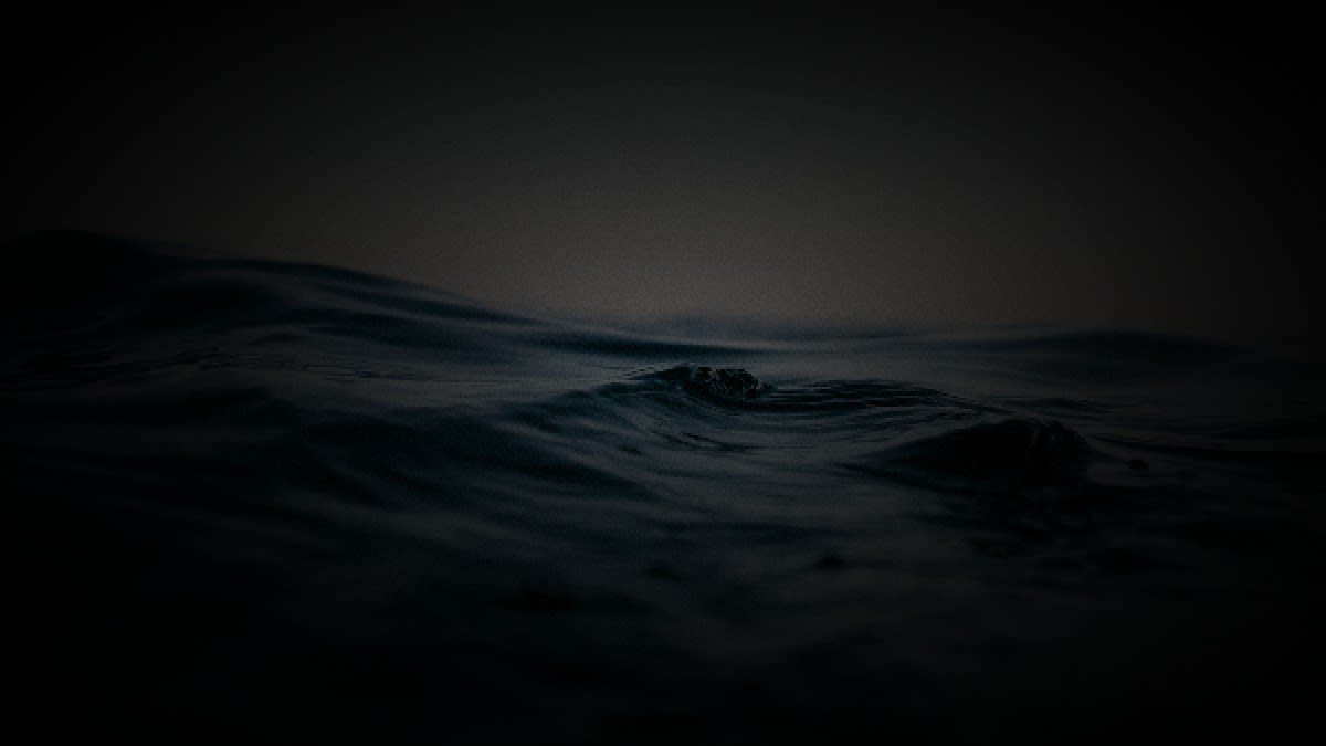 Photorealistic editorial photo of dark Atlantic water at dusk with a soft fog bank on the horizon and cold natural light, no people.