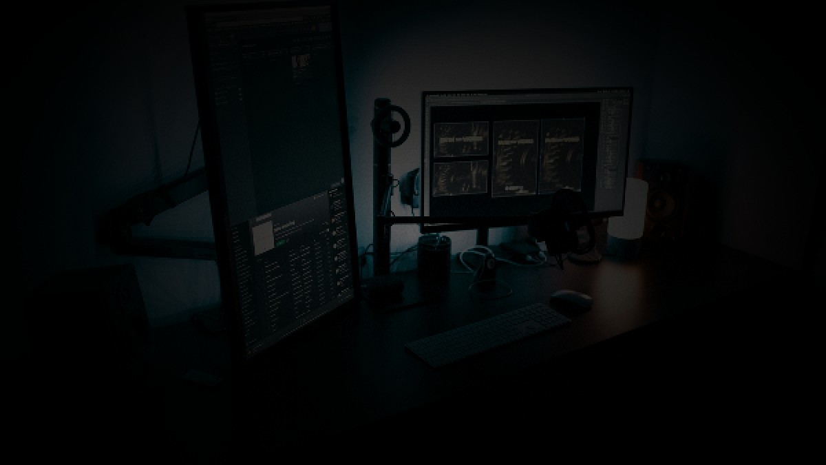 Photorealistic editorial photo of an empty high-tech dual-monitor desk at night with cool cyan backlight and warm desk lamp, no people.