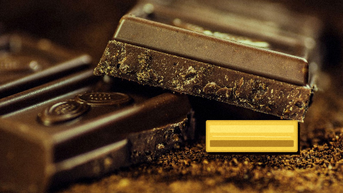 Photorealistic editorial macro of dark chocolate shards with a face-down golden foil ticket prop under warm tungsten light, no text readable.