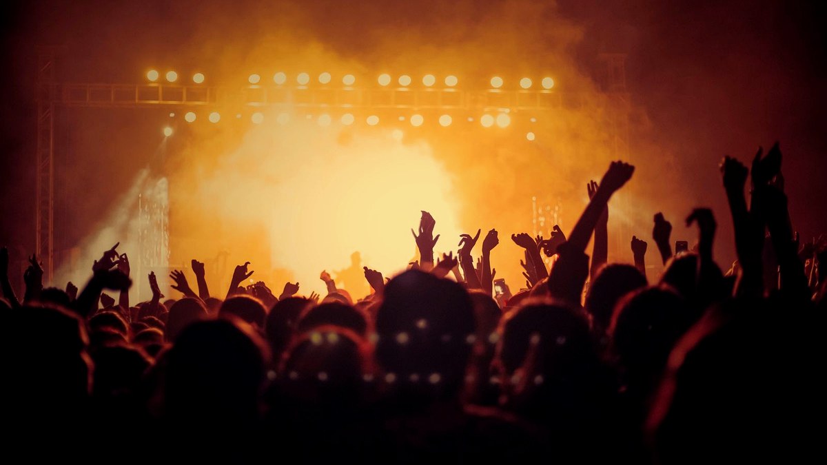 Editorial cover: concert stage lights and silhouetted crowd under warm haze for SNL Dakota Johnson Turnstile Oct 3.