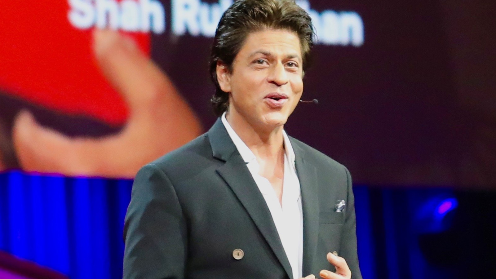 Actor Shah Rukh Khan speaking on stage in a green jacket