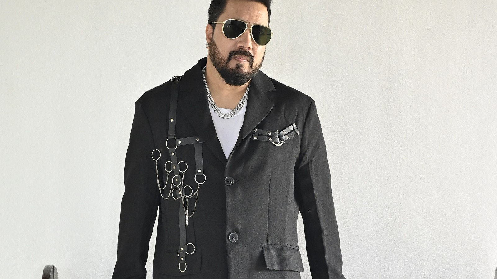 Singer Mika Singh in a black jacket and sunglasses against a white backdrop