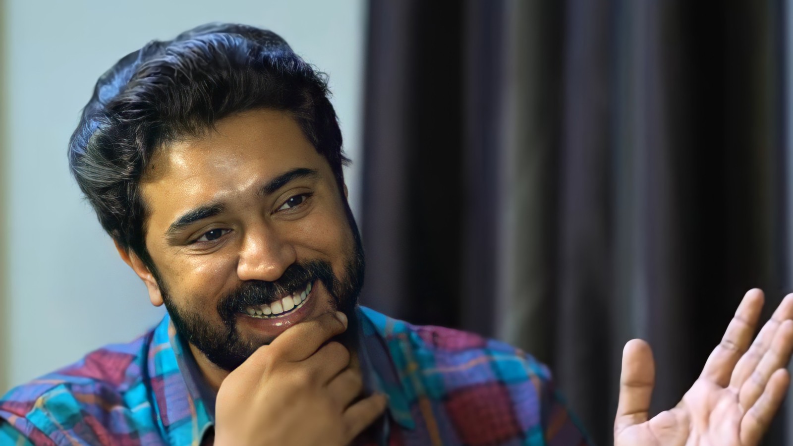 Actor Nivin Pauly laughing with his hand on his chin