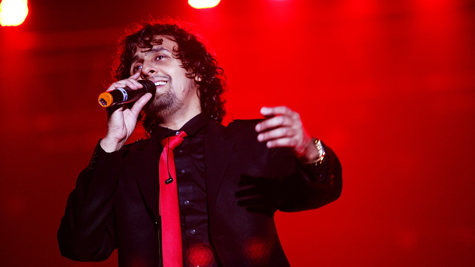 Singer Sonu Nigam performing on stage in a dark jacket and red tie