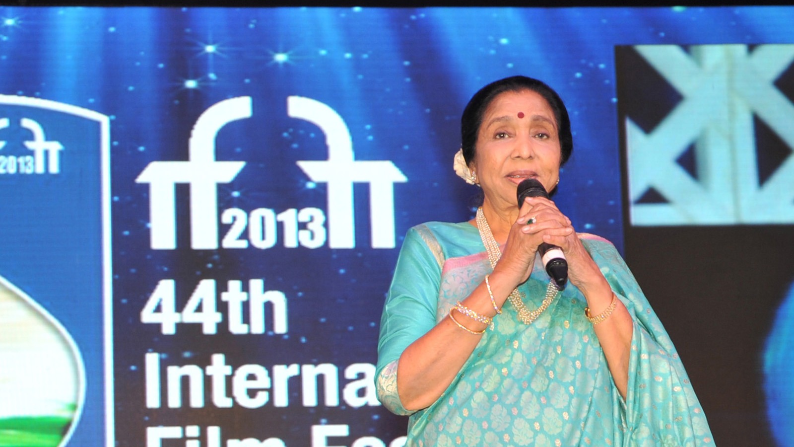 Singer Asha Bhosle holding a microphone and addressing the 2013 International Film Festival of India