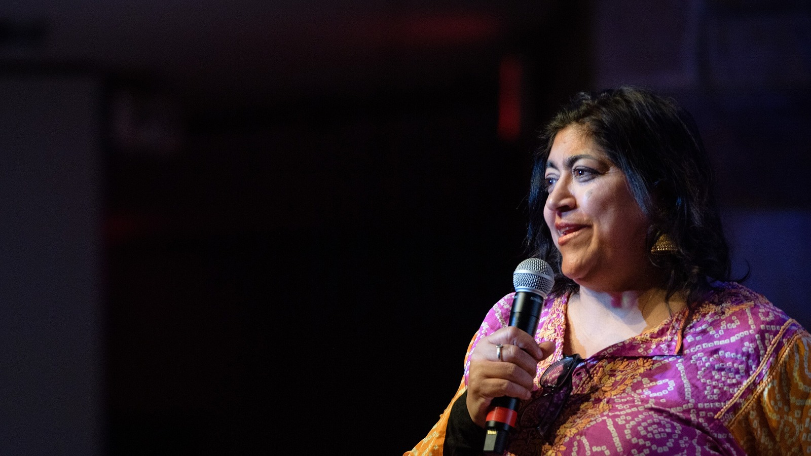 Director Gurinder Chadha speaking into a microphone in a bright patterned top
