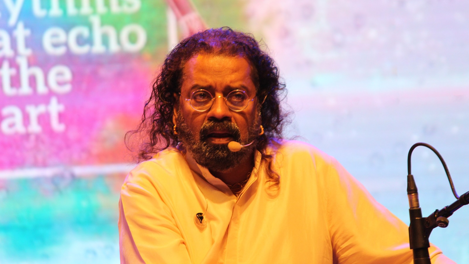 Singer Hariharan with long hair and glasses in an orange kurta performing on stage