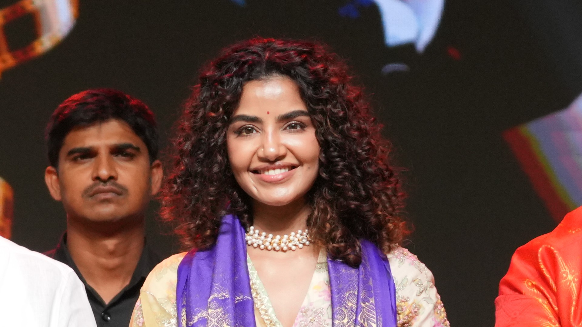 Actor Anupama Parameswaran smiling in a purple stole and pearl necklace on stage with the Crazy Kalyanam team